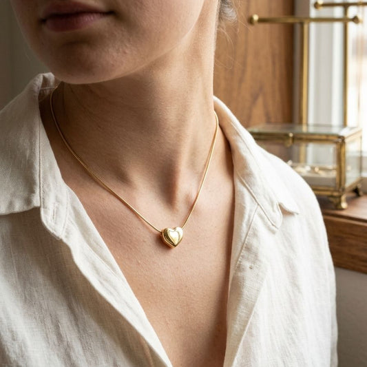 Person wearing a gold heart-shaped necklace in a softly lit room.