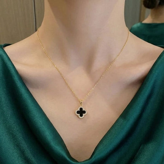 Gold necklace with a clover-shaped pendant on a person wearing a green top.