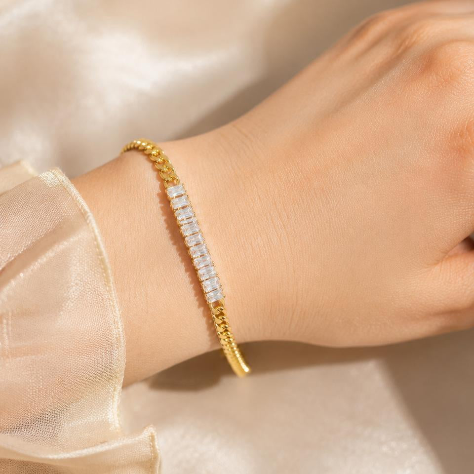 Gold bracelet with clear stones on a wrist against a beige fabric background