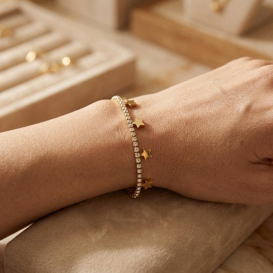 Gold bracelet with star charms on a wrist, with a jewelry box in the background