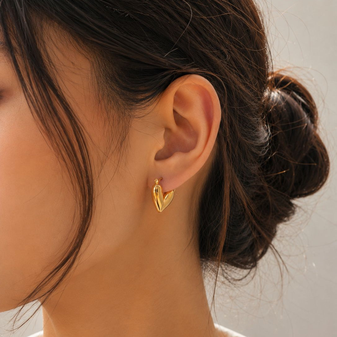 Close-up of a person wearing a gold heart-shaped earring against a neutral background