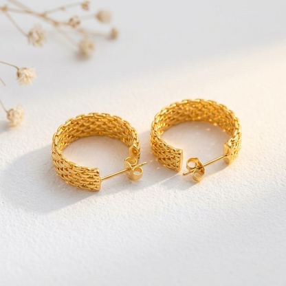 Pair of gold hoop earrings on a white background with dried flowers.