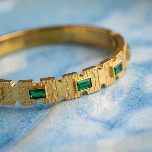 Gold bracelet with green gemstones on a blue marble surface
