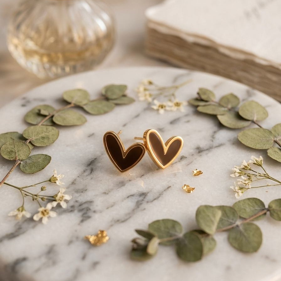 Heart-shaped earrings on a marble surface with green leaves and a book in the background
