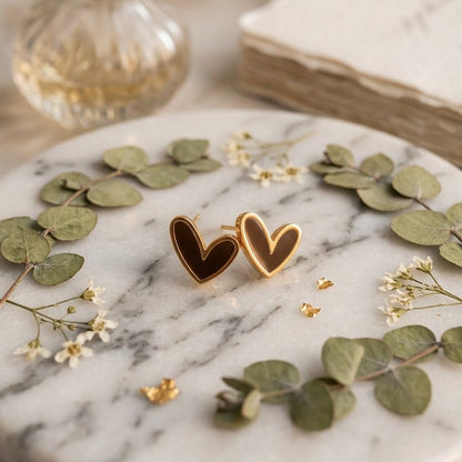 Heart-shaped earrings on a marble surface with green leaves and a book in the background