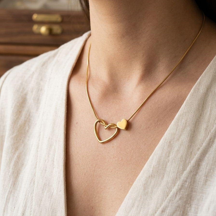 Gold necklace with a heart pendant worn by a person in a light-colored outfit.