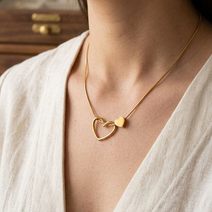 Gold necklace with a heart pendant worn by a person in a light-colored outfit.