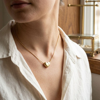 Person wearing a gold heart-shaped necklace in a softly lit room.