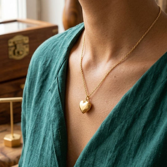 Person wearing a gold heart-shaped necklace with a blurred background