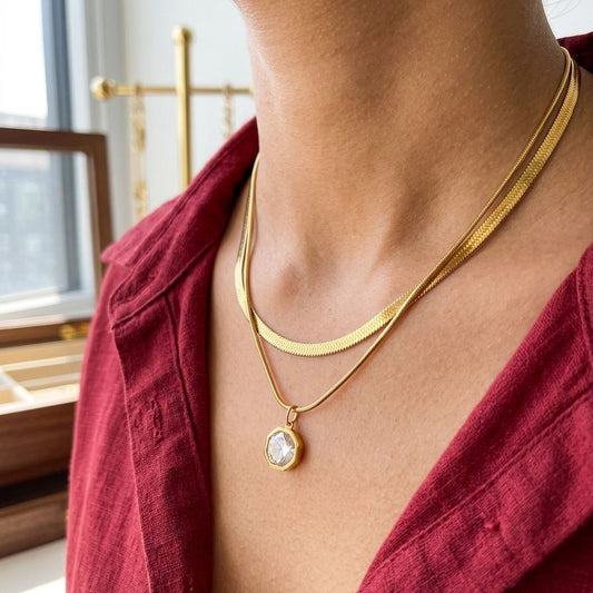 Person wearing a gold necklace with a pendant in a room with a window and furniture.