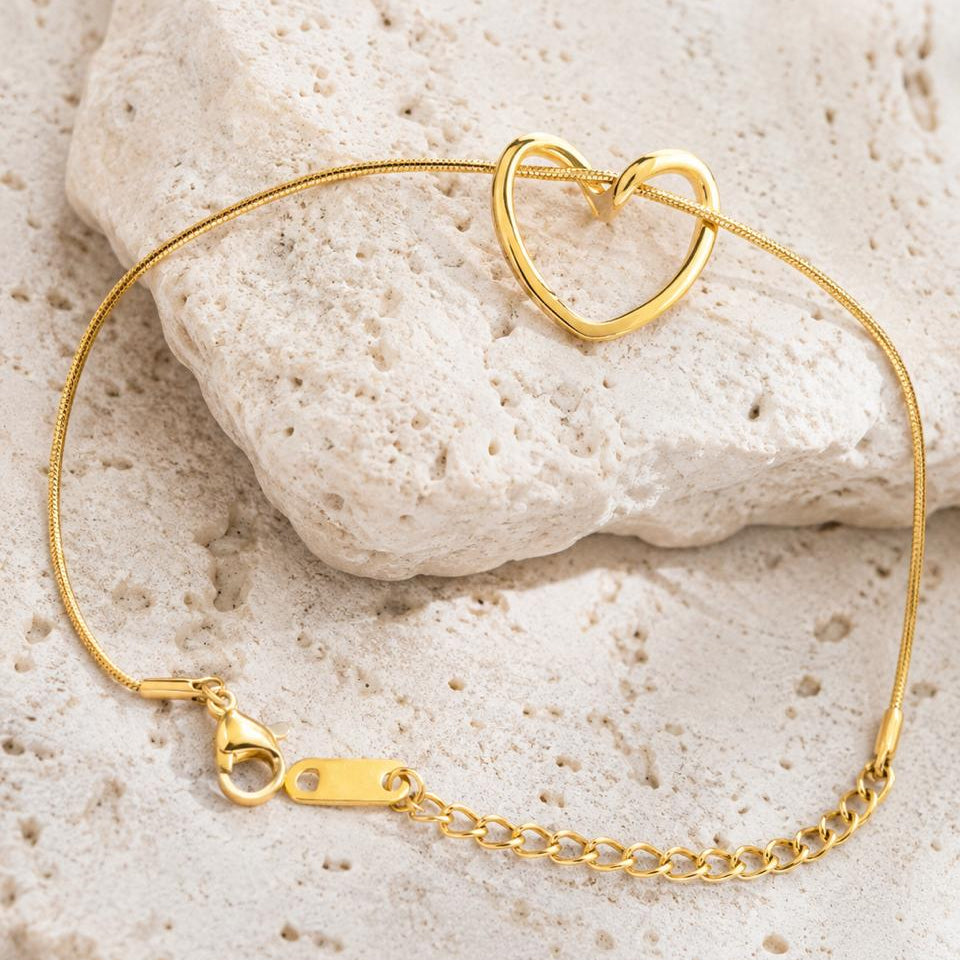 Gold bracelet with a heart-shaped clasp on a stone surface