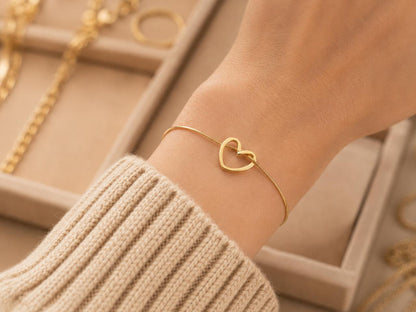 Gold heart-shaped bracelet on a wrist with a neutral background