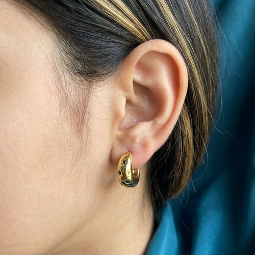 Gold hoop earring worn by a person with a blue background