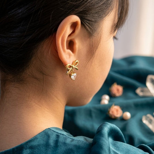 Close-up of a person wearing a gold bow-shaped earring with a blurred background