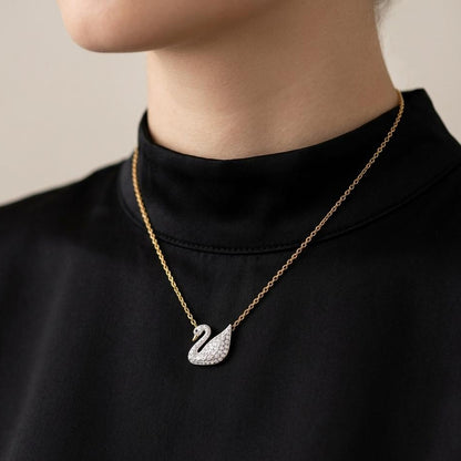 Gold necklace with a swan pendant worn by a person against a neutral background