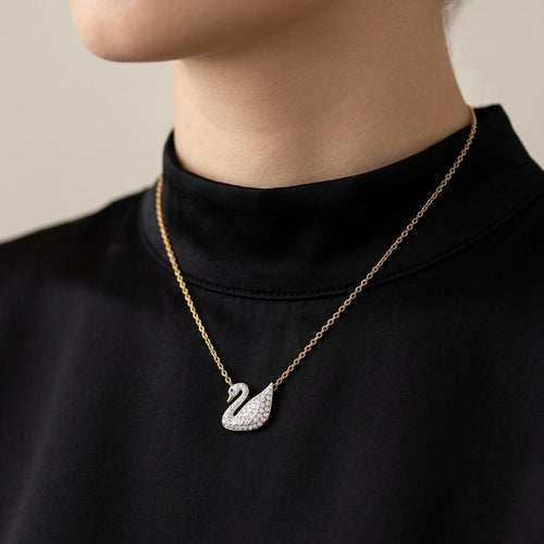 Gold necklace with a swan pendant worn by a person against a neutral background
