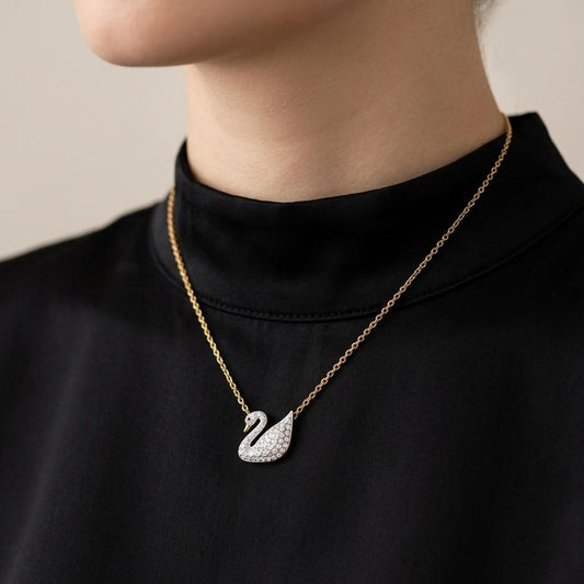 Gold necklace with a swan pendant worn by a person against a neutral background